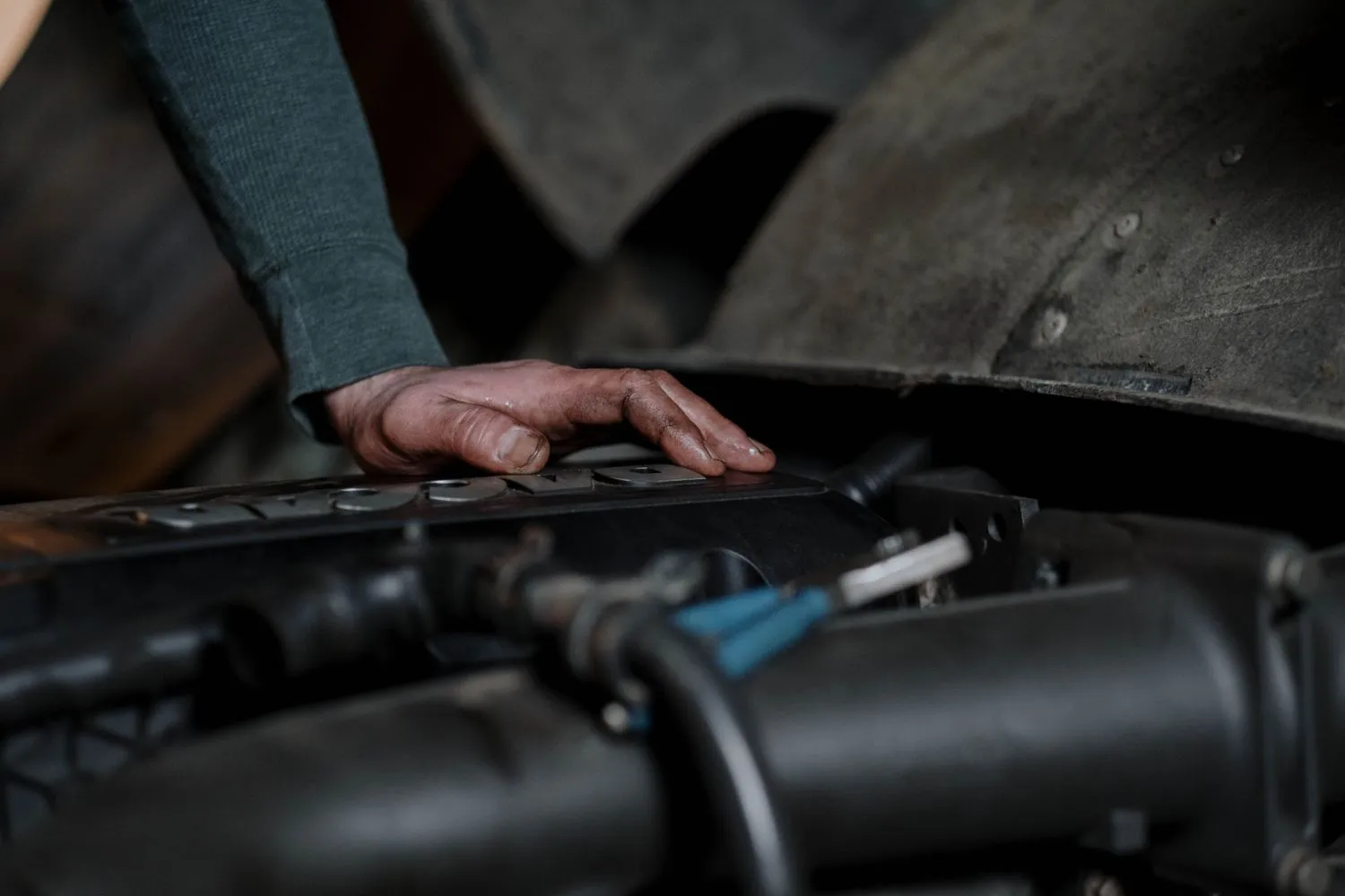 Mecanic cu mâna pe blocul motor, într-un atelier întunecat